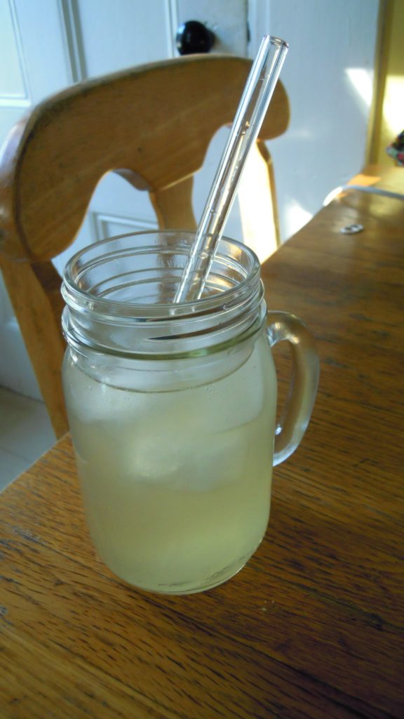 A photo of a mason jar on a table, filled with margarita and topped with a Glass Dharma drinking straw.