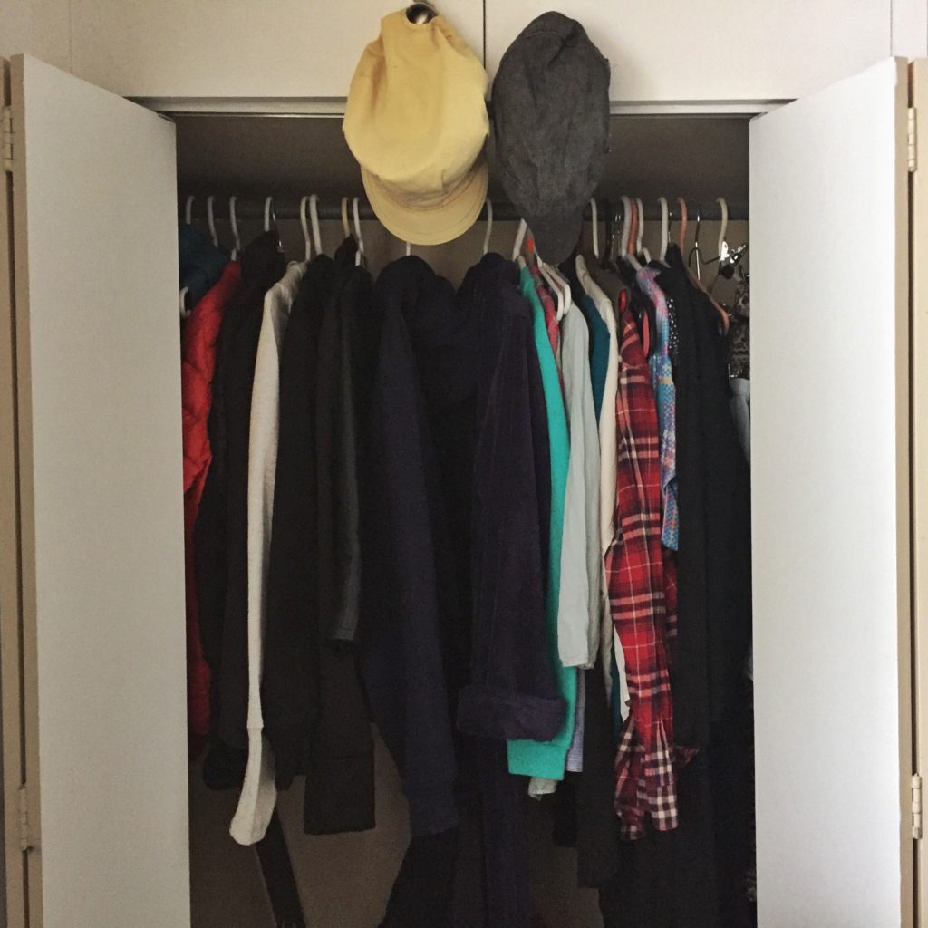 clothing hung in a closet with hats before a closet cleanout