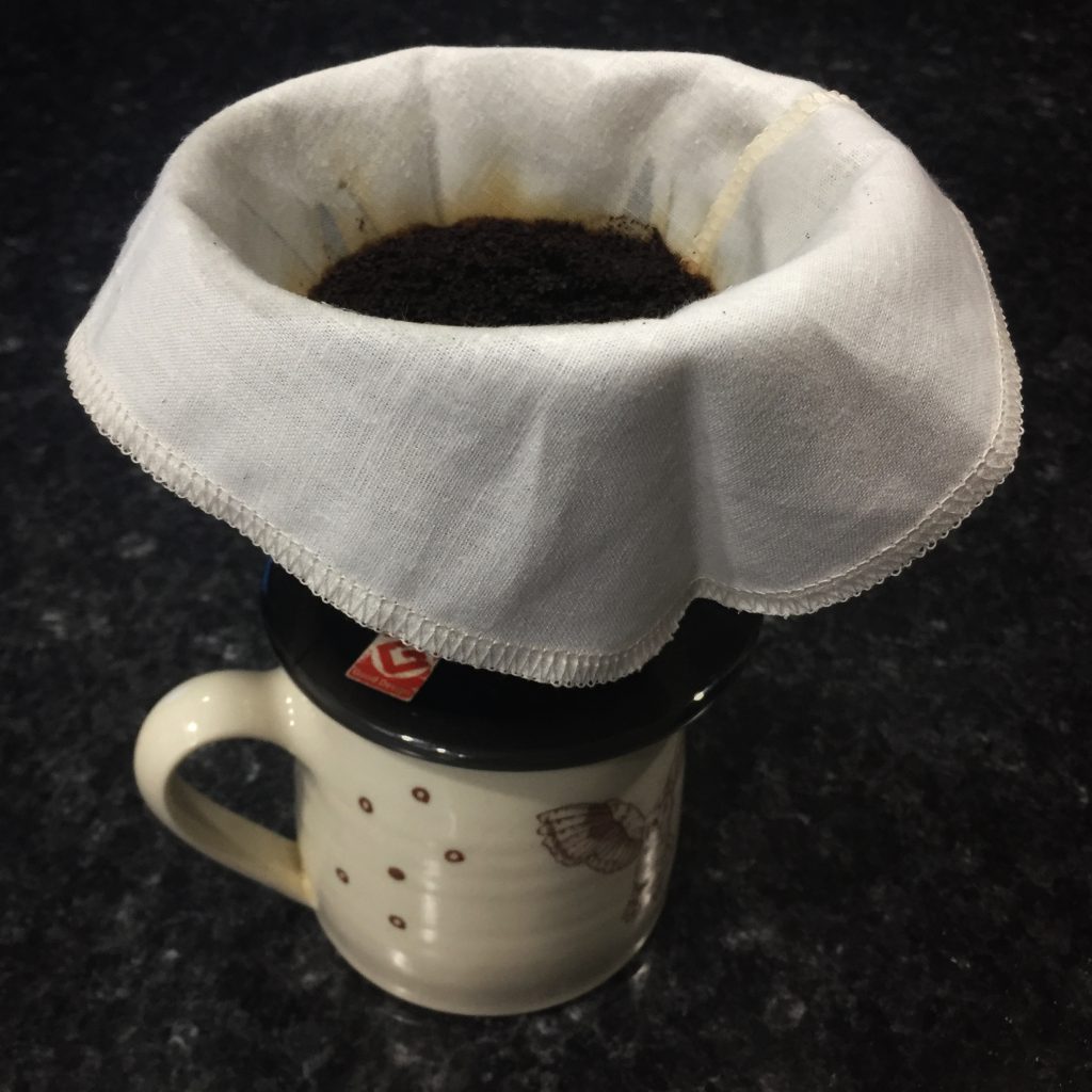 image of a cone-style coffee brewer sitting on top of a mug with a reusable Pinyon Products-brand filter full of coffee grounds