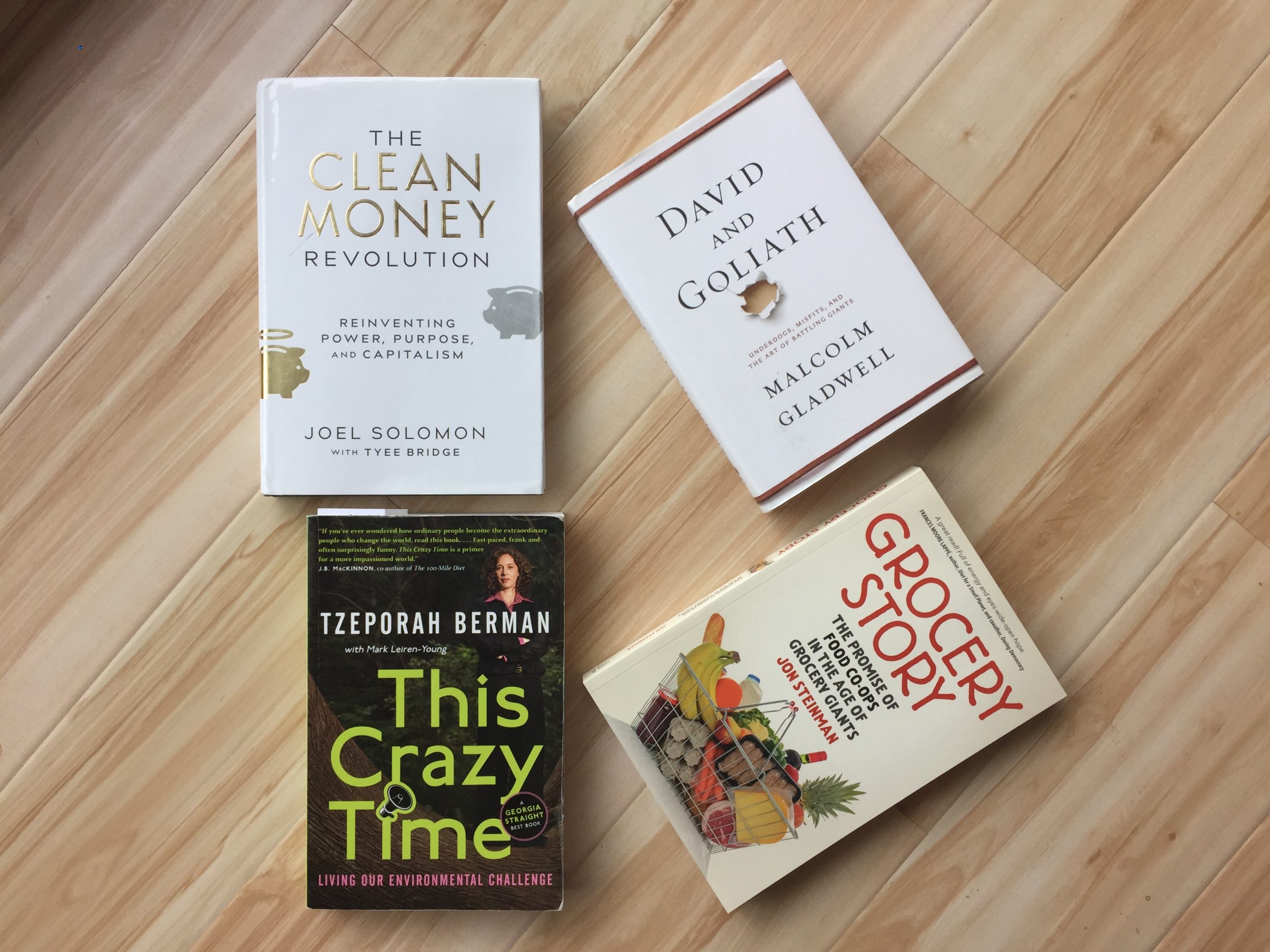 green-themed books that tackle sustainability topics with collaboration in mind, all written by Canadian authors. Titles include: clean money revolution by joel solomon, david and goliath by malcolm gladwell, this crazy time by tzeporah berman, and grocery story by jon steinman.