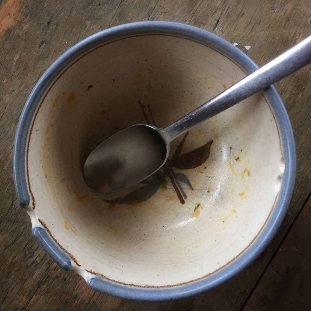 an empty ceramic bowl with a stainless steel spoon that previously held garden vegetable soup.