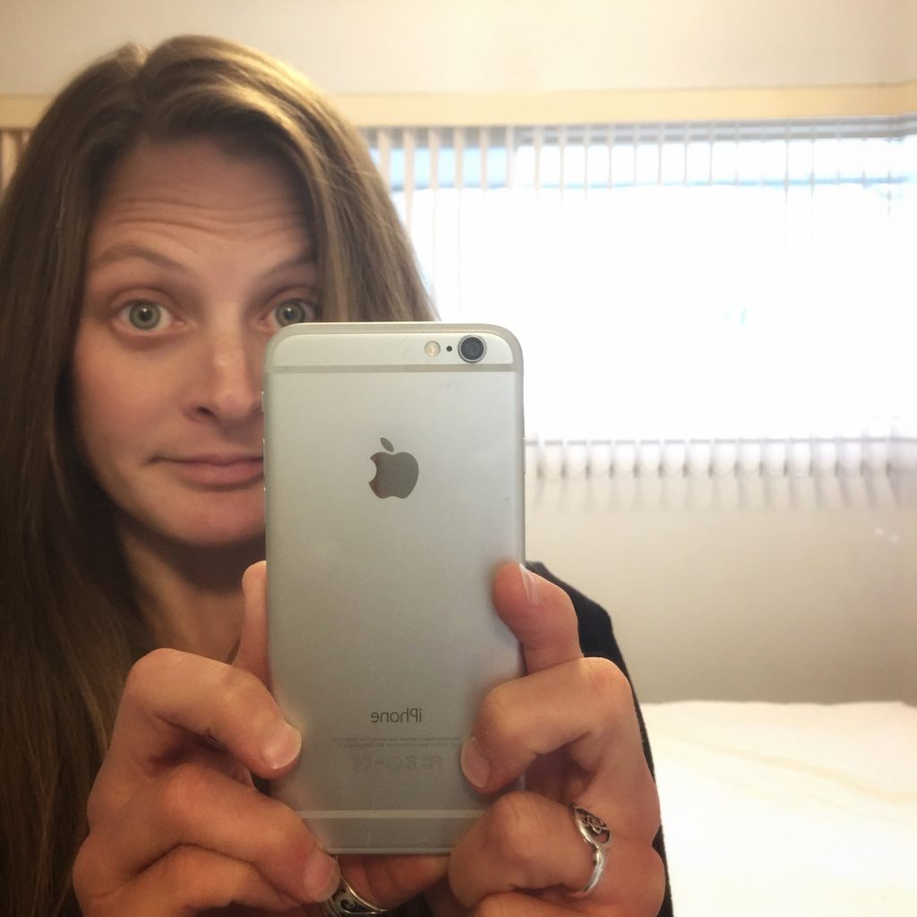 A mirror-selfie image of the author holding her seven-year-old iphone 6. Not pictured: the screen and battery repair jobs she undertook by herself using kits, instead of replacing.