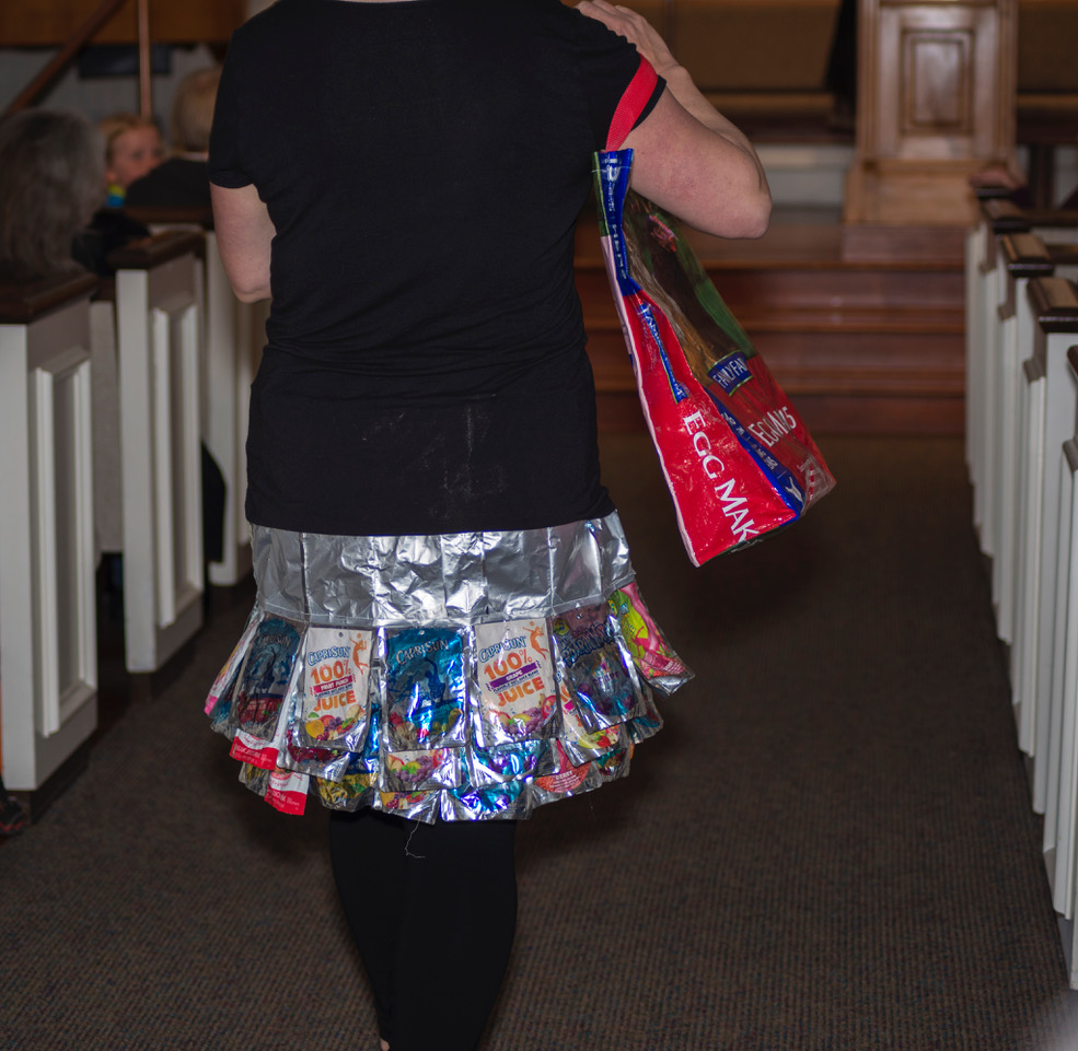 Deb Rudnick walks down an aisle modelling a skirt and handbag made from discarded materials.