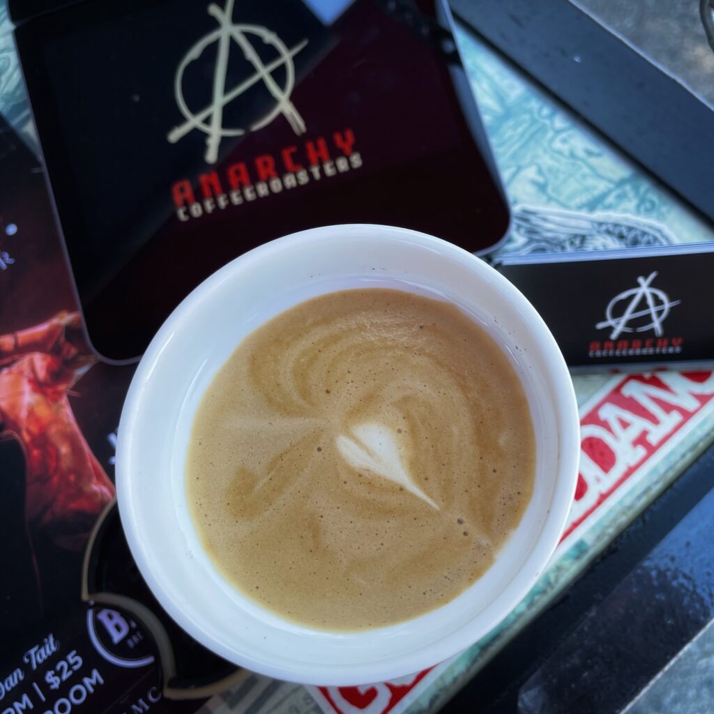 Low-waste living means buying coffee in reusable mugs. This cup of coffee is from Anarchy Coffee Roasters and has a small, white heart on top!