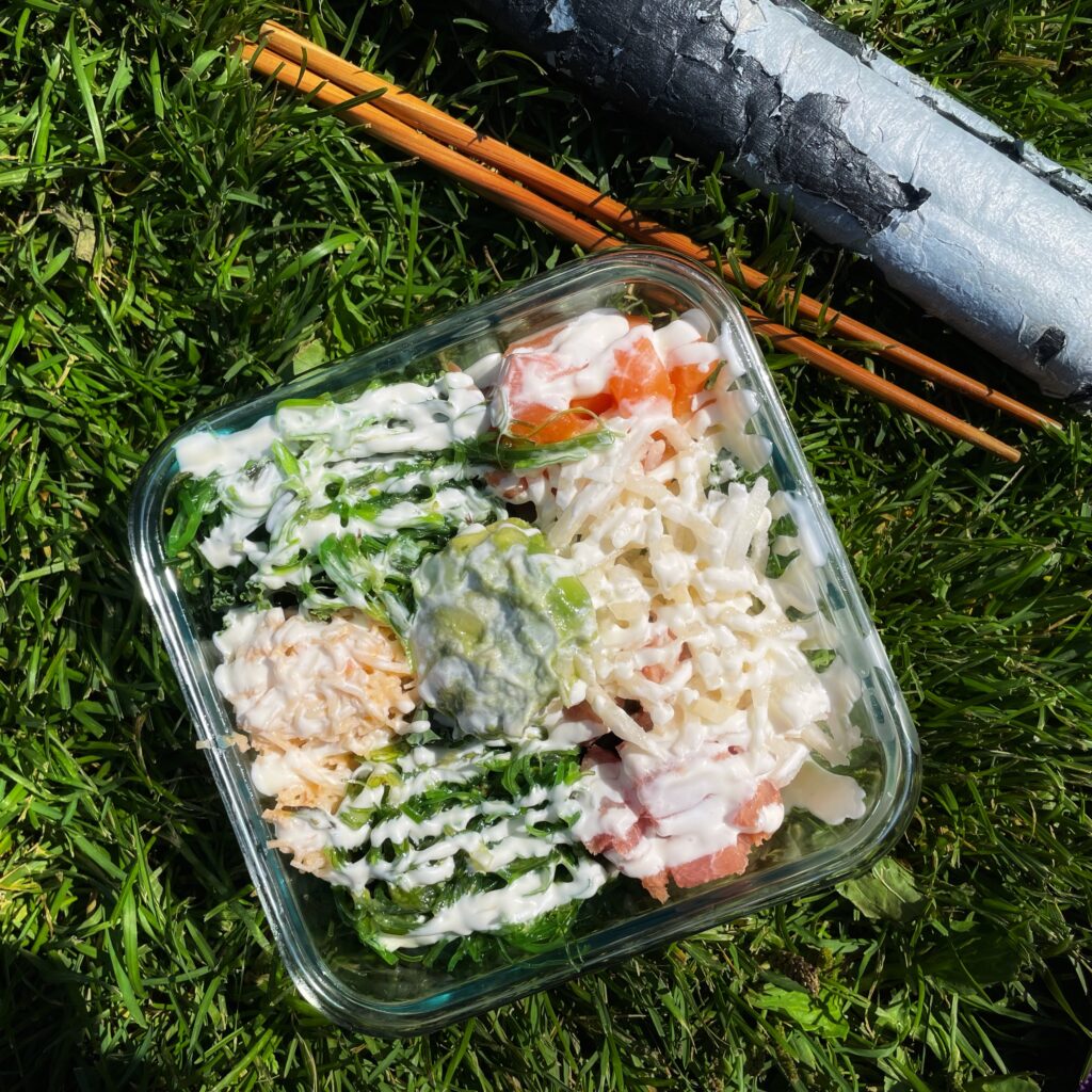 A top-down view of the author's zero-waste picnic poke bowl lunch, in a glass container next to a set of reusable bamboo chopsticks.