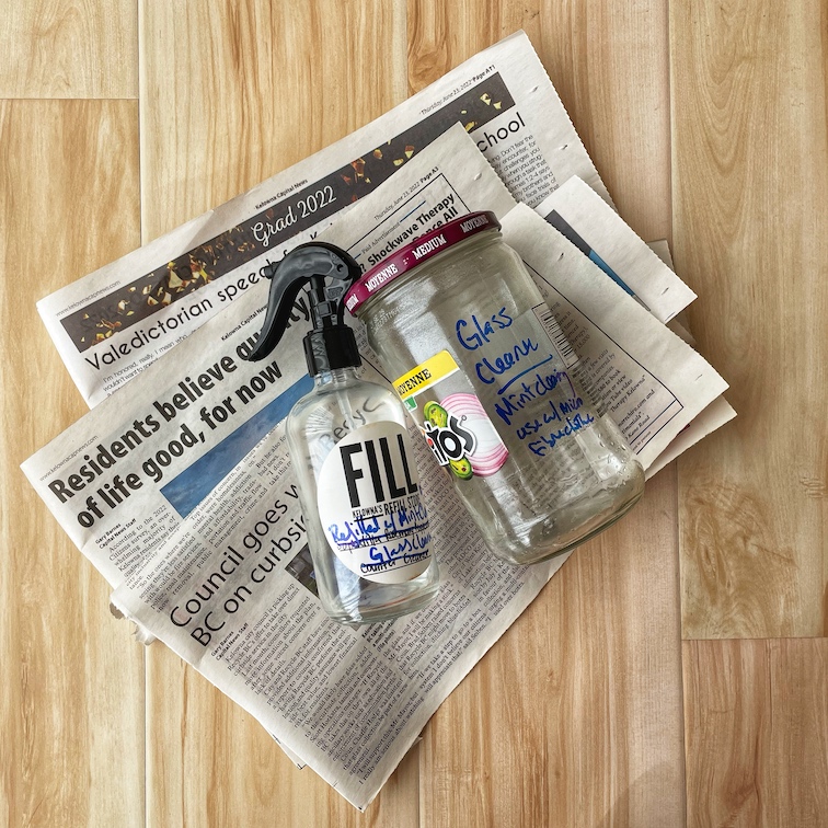 Two jars of earth-friendly glass cleaner lay on top of a pile of newspapers on the floor.