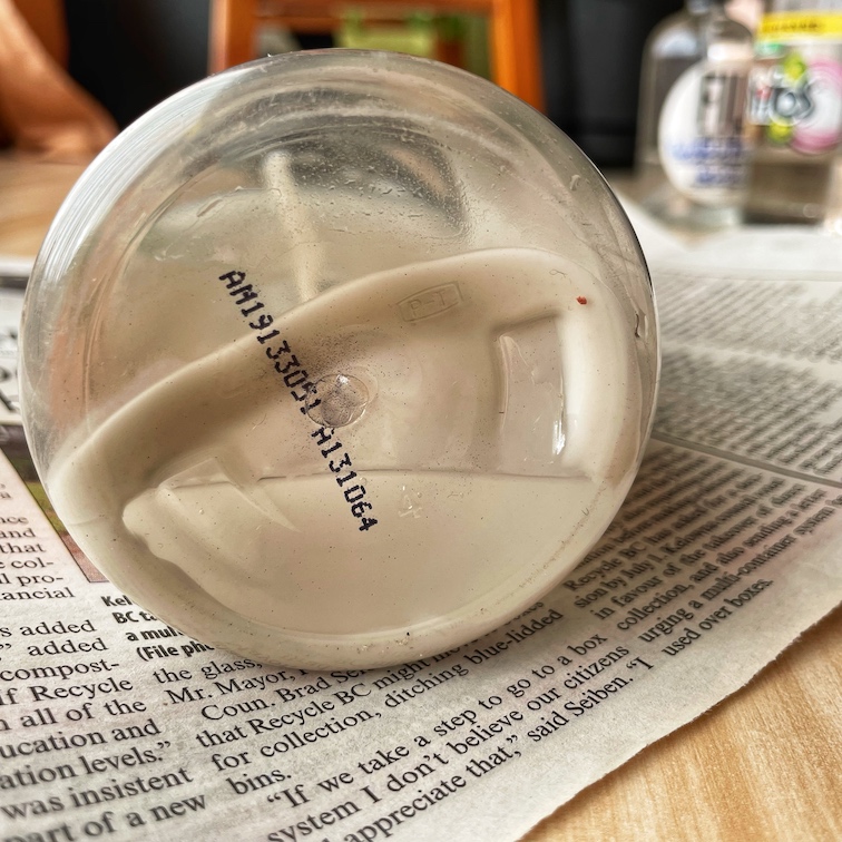 A close-up of the bottom of a bottle of DIY glass cleaner showing the cornstarch accumulating, while the bottle lays on top newspapers.