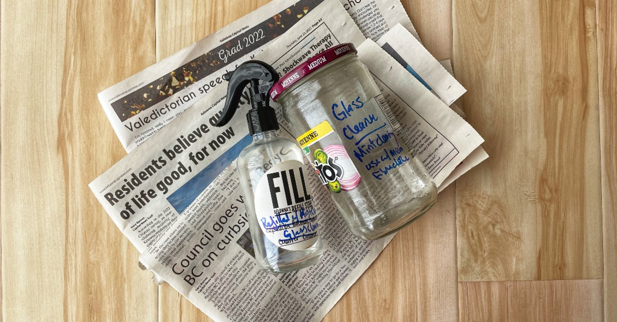 Two jars of earth-friendly glass cleaner lay on top of a pile of newspapers on the floor.