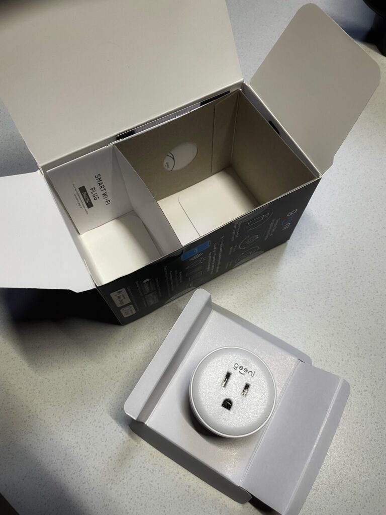 Geeni smart plug packaging, shown with the Smart Plug product sitting outside of the box.