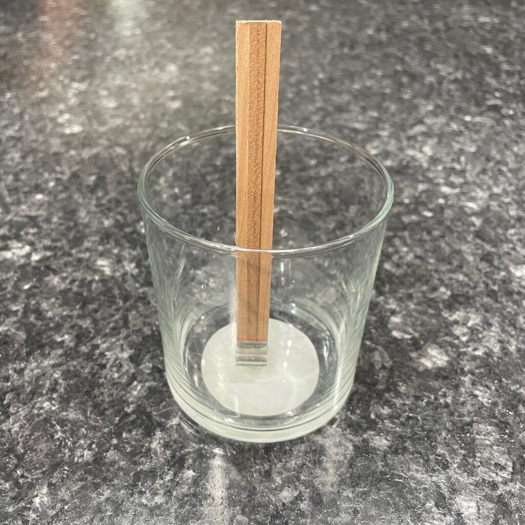 An empty glass candle jar with a wooden wick standing in the middle of it.