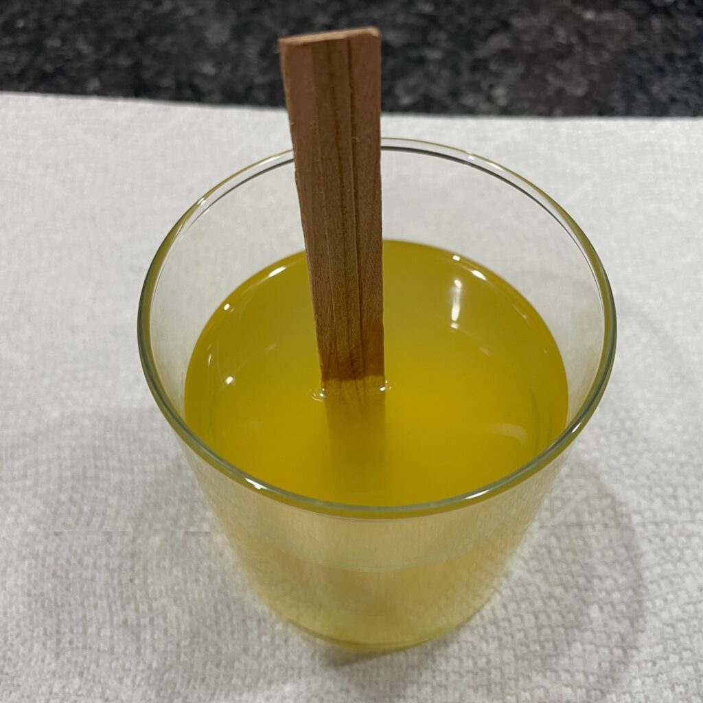 A reused glass candle jar with new melted, yellow candle wax and a wooden wick in the middle.