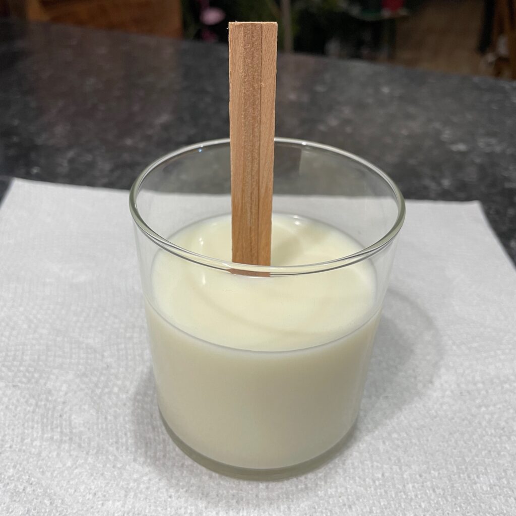 A reused glass candle jar with new, solid candle wax and a wooden wick in the middle.