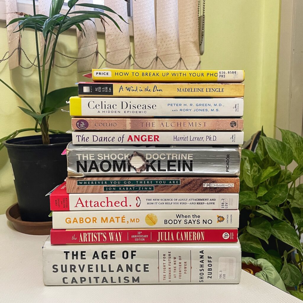 A stack of books to read in Q1 with green plants behind it.