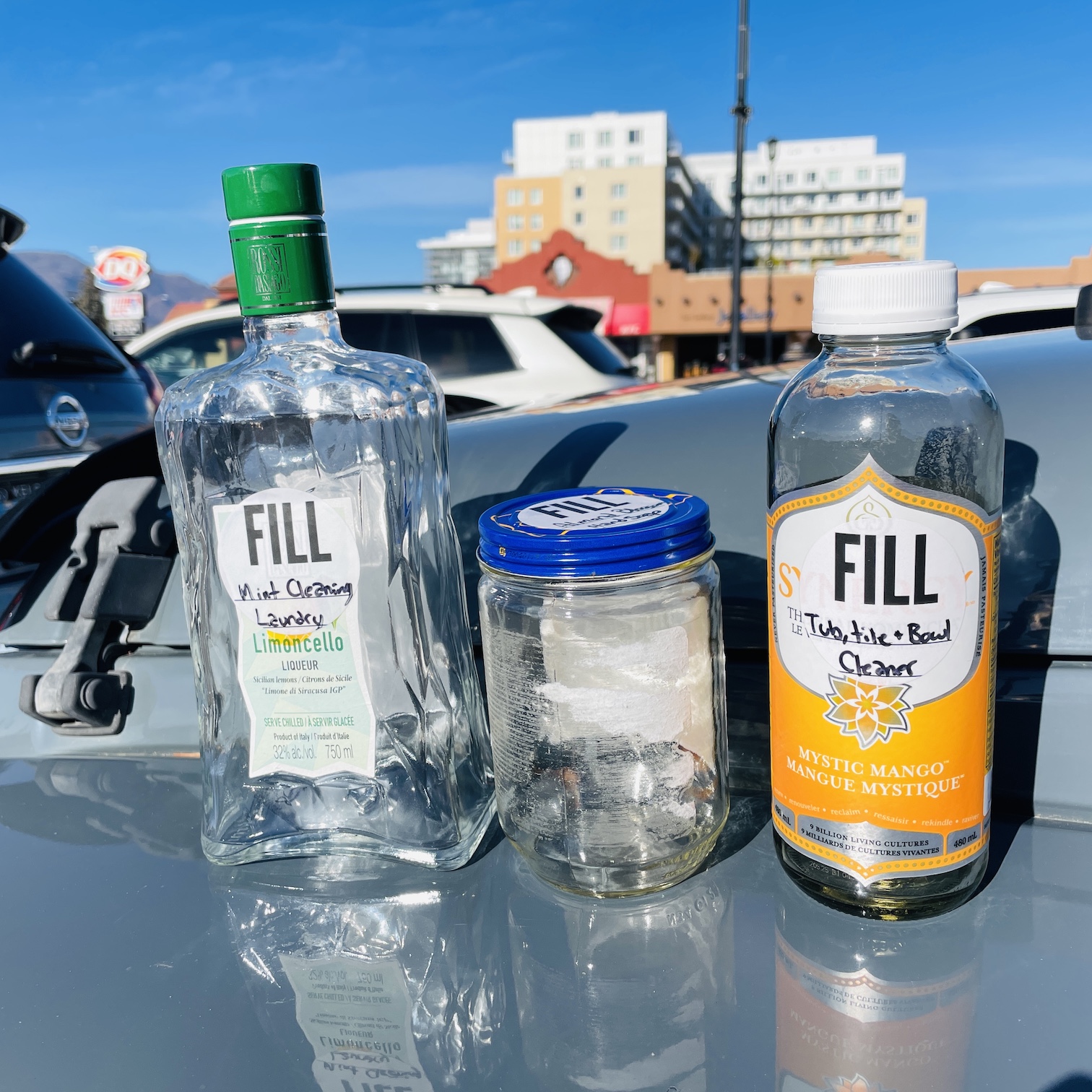 A variety of empty glass bottles sits on top of a car hood.