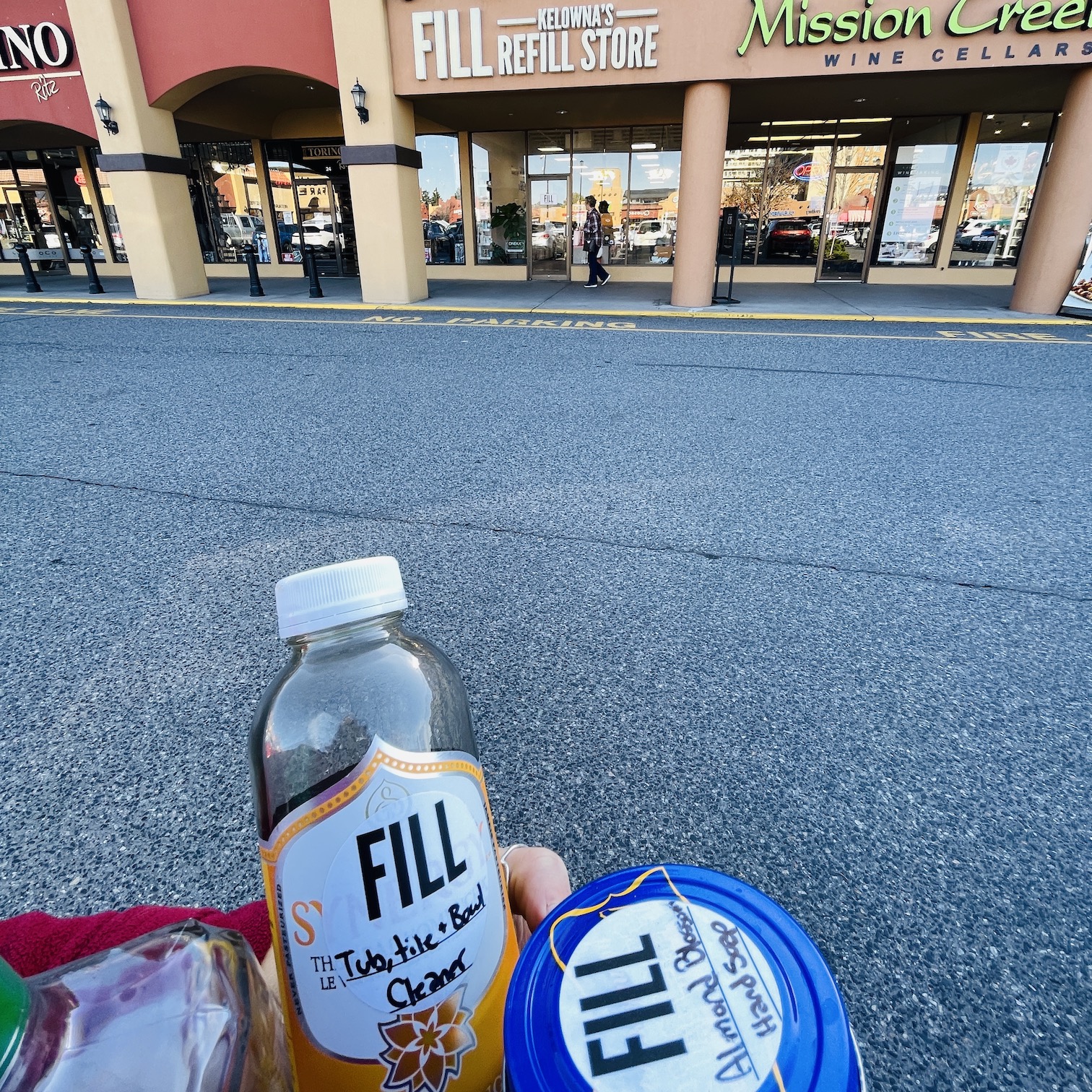 A variety of glass jars shown in the foreground, with FILL Kelowna's Refill Store in the background.