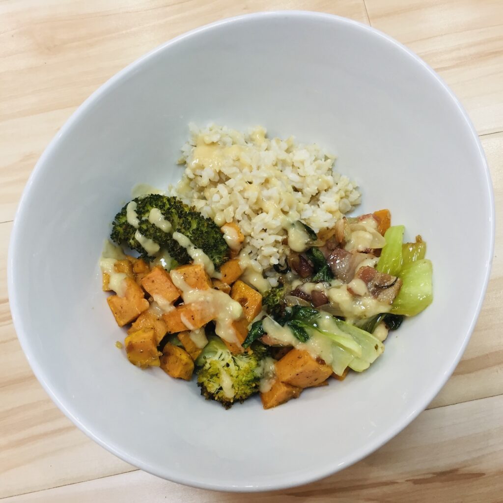 A top-down image of a white bowl filled with brown rice and roasted yams and broccoli.