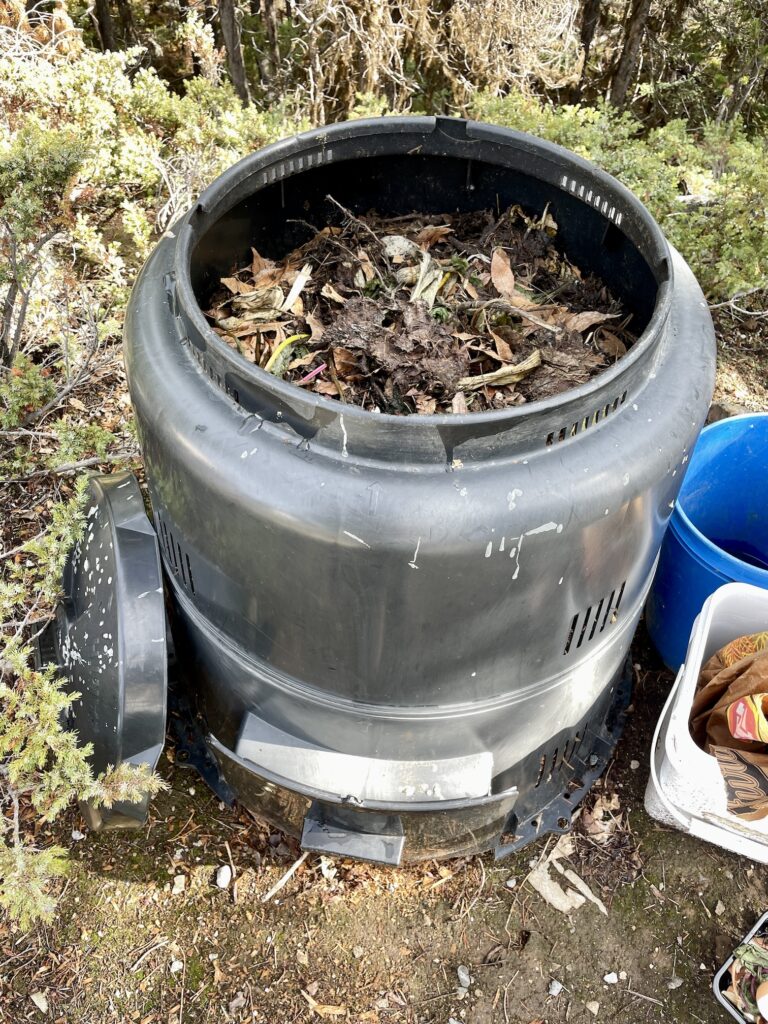 A black plastic home composter is shown with its lid off, revealing a pile that reaches almost to the brim.