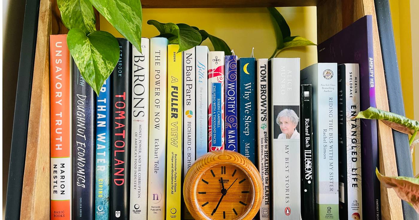 The author's bookshelf featuring an assortment of titles, with a wooden clock sitting in the middle, and various green plants on the edges.